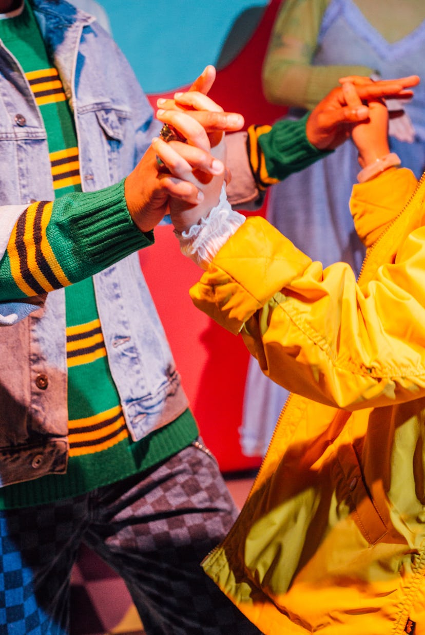 Three people wearing colorful outfits making hand gestures, focusing on their stylish clothes and ha...