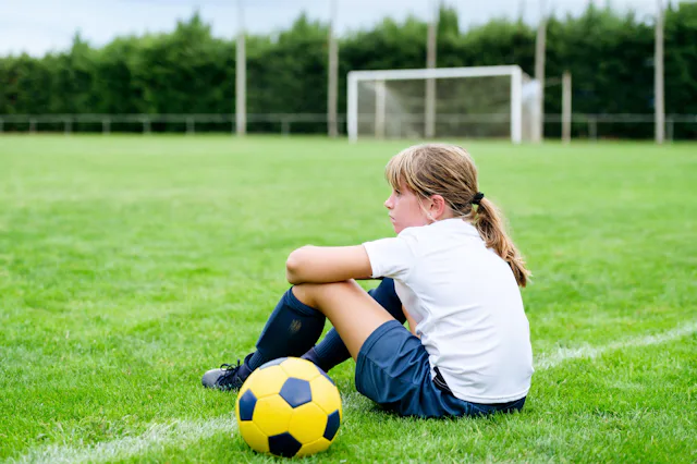 A young soccer player sits on a field, defeated.