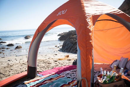 Orange beach tent set up on sandy beach with view of the ocean, rocky shoreline visible in the backg...