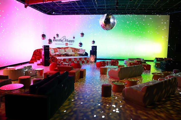 Colorful party room with round tables, plush seating, and a birthday cake setup under a disco ball a...
