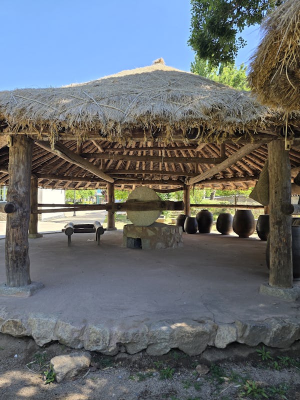 Thatched roof pavilion with traditional stone and pottery vessels displayed at Gyeongbokgung Palace….
