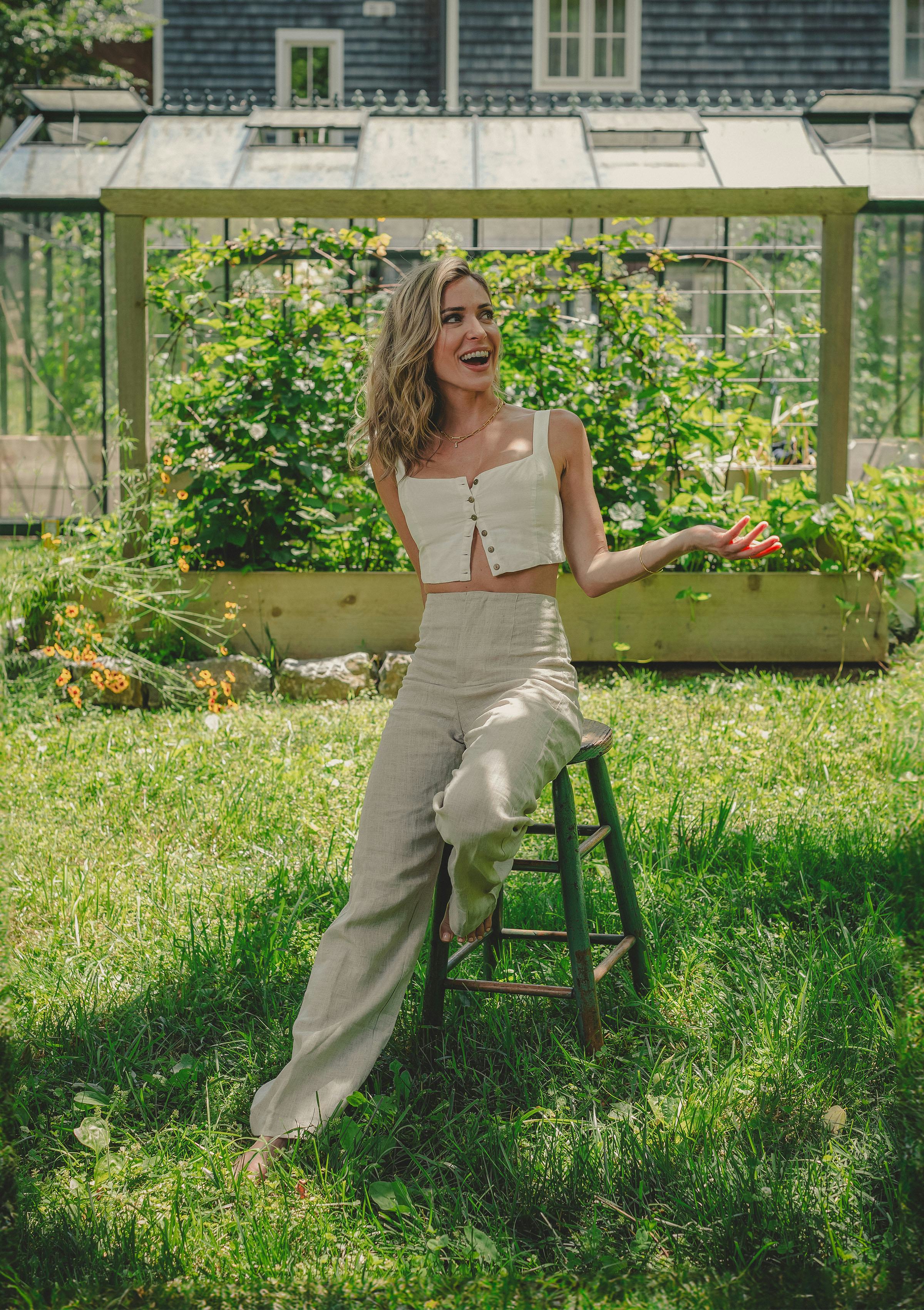 Kristin Cavallari poses on a stool in front of a vegetable garden.