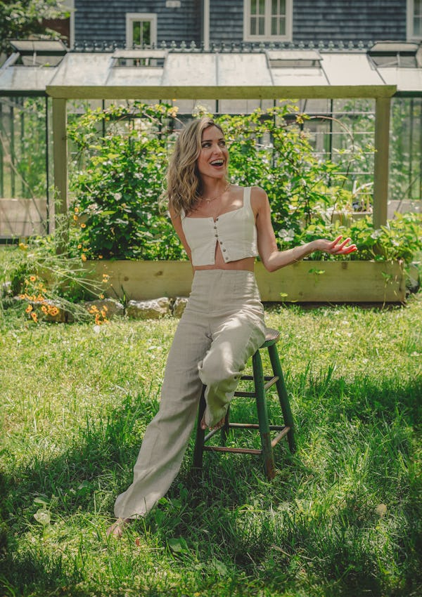 Kristin Cavallari poses on a stool in front of a vegetable garden.