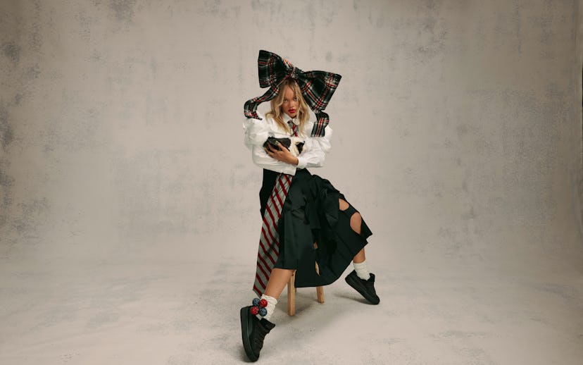 A stylish woman in a large checkered bow, ruffled blouse, and striped skirt poses while looking at a...