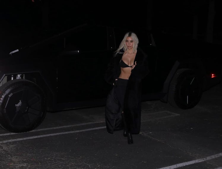 Kim Kardashian walking through a parking area with a long coat and bra top