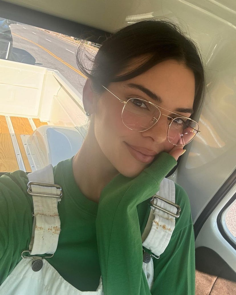 Kendall Jenner wears cream overalls with a green sweatshirt.