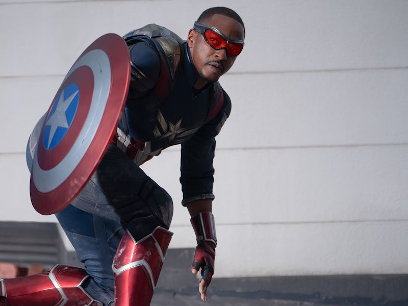 Sam Wilson as Captain America, wearing a suit with shield, crouches ready for action against a build...