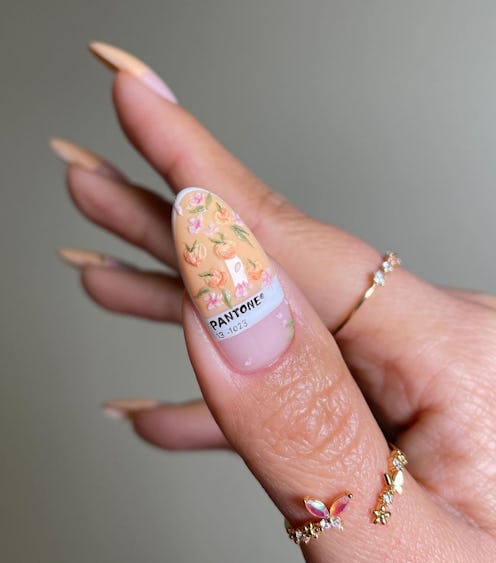 Close-up of a hand with long, almond-shaped nails painted in a delicate floral design, featuring a P...