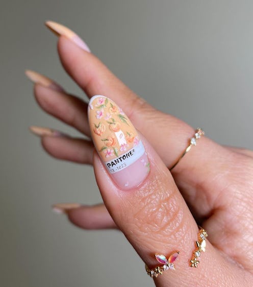 Close-up of a hand with long, almond-shaped nails painted in a delicate floral design, featuring a P...
