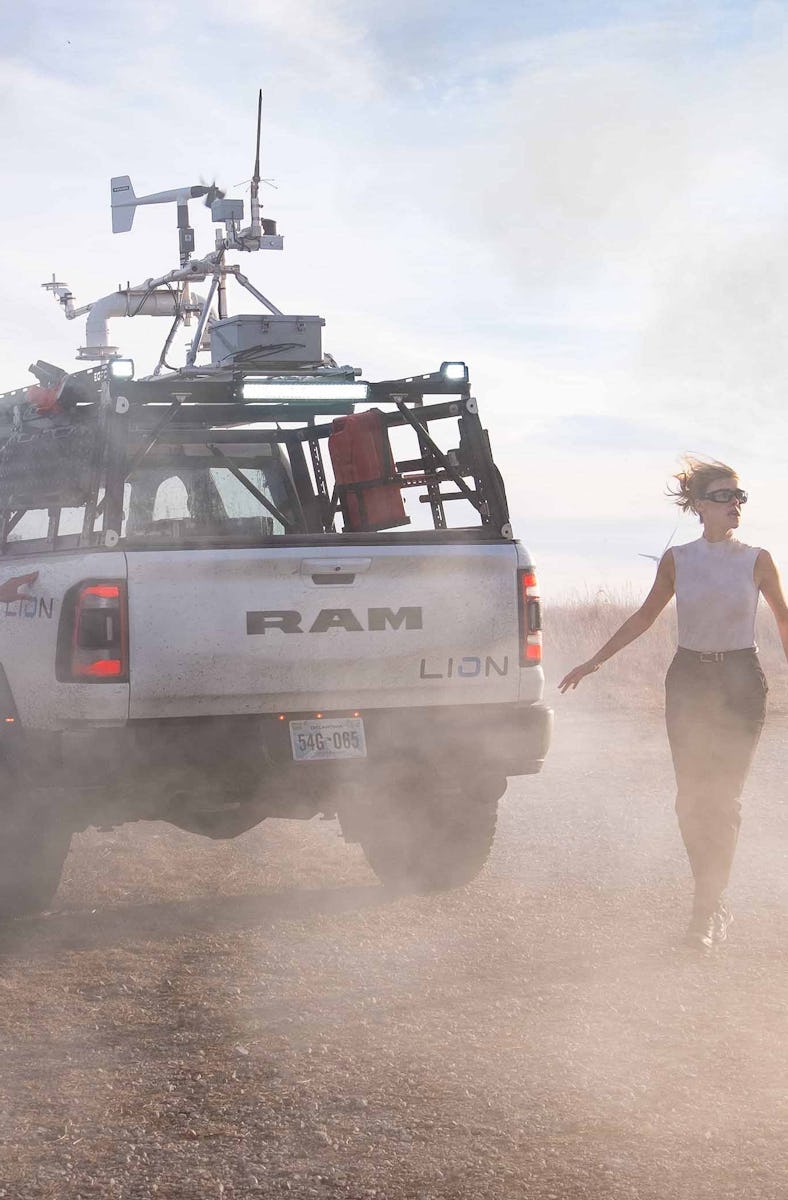 A dusty scene with two people and a truck equipped with technical gear in a barren landscape, creati...
