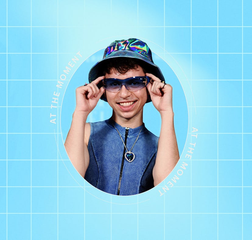 Young man wearing a colorful hat and sunglasses smiles playfully against a blue grid background.