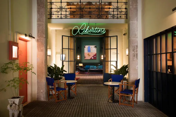 Elegant entrance to the "Libertine" lounge with tiled floor, green neon sign, open doors, and stylis...