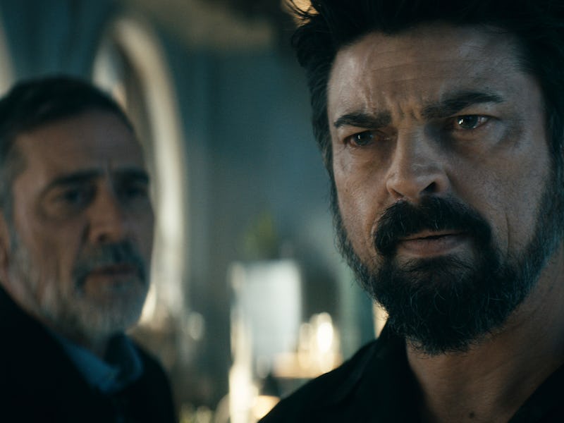 Two men with serious expressions in a dimly lit room, one with a beard looking forward intently, the...