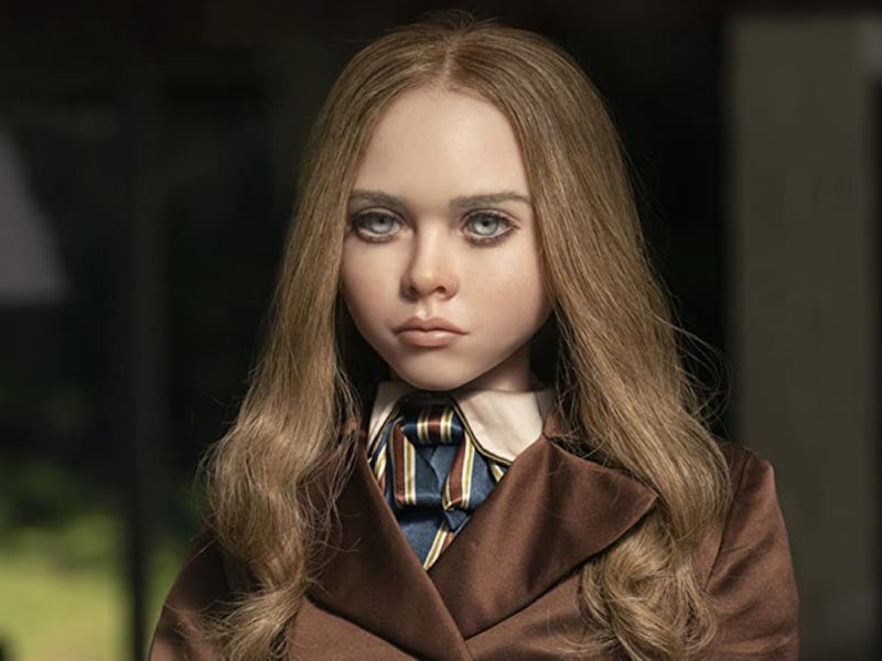 A young girl with blonde hair and serious expression, wearing a brown jacket and a striped tie, sitt...