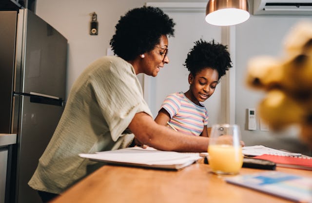 A woman and a young girl engaged in studying at a kitchen table, with books and a glass of juice vis...