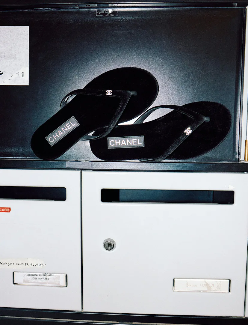Black designer flip flops with logo placed on top of a gray office storage locker.