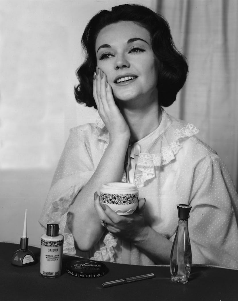 circa 1965: A woman wearing a night gown smiles as she applies Satura moisturizing lotion and cold c...