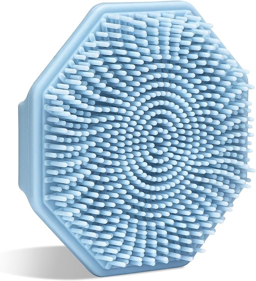 A blue, hexagonal silicone brush mat with a spiral pattern of soft bristles, isolated on a white bac...