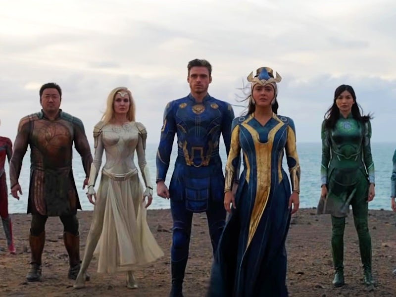 Group of diverse superheroes in colorful costumes standing on a beach with a cloudy sky in the backg...
