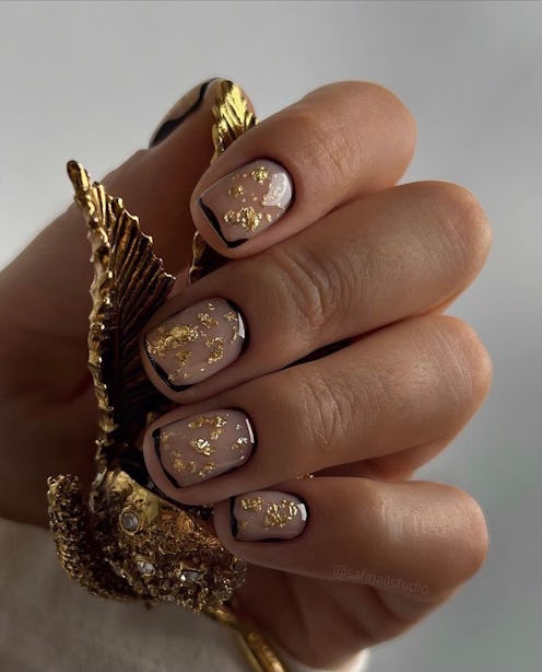 Elegant taupe manicured nails with gold flake accents, held against a detailed gold seashell.