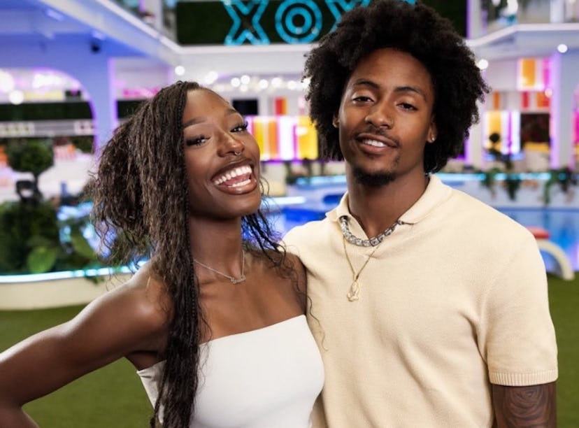 A cheerful couple posing with smiles in a colorful room with neon lighting and "XOXO" sign in the ba...
