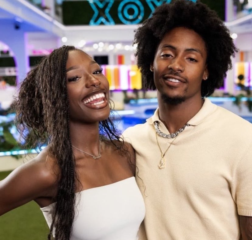 A cheerful couple posing with smiles in a colorful room with neon lighting and "XOXO" sign in the ba...