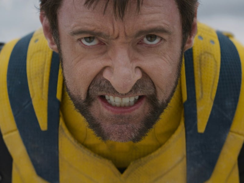 Man with intense expression wearing a yellow and blue superhero suit, crouching forward as if ready ...