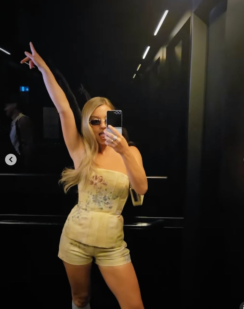 Sydney Sweeney posing for a selfie with her arm up wearing a floral bustier top.