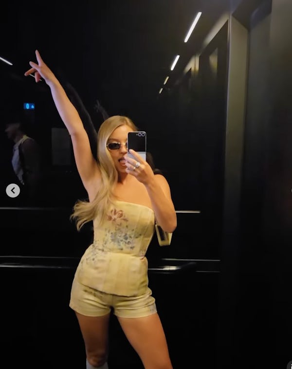 Sydney Sweeney posing for a selfie with her arm up wearing a floral bustier top.