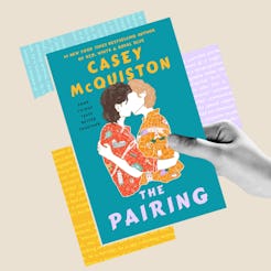 Hand holding the book “The Pairing” by Casey McQuiston, featuring an illustrated cover with two peop…