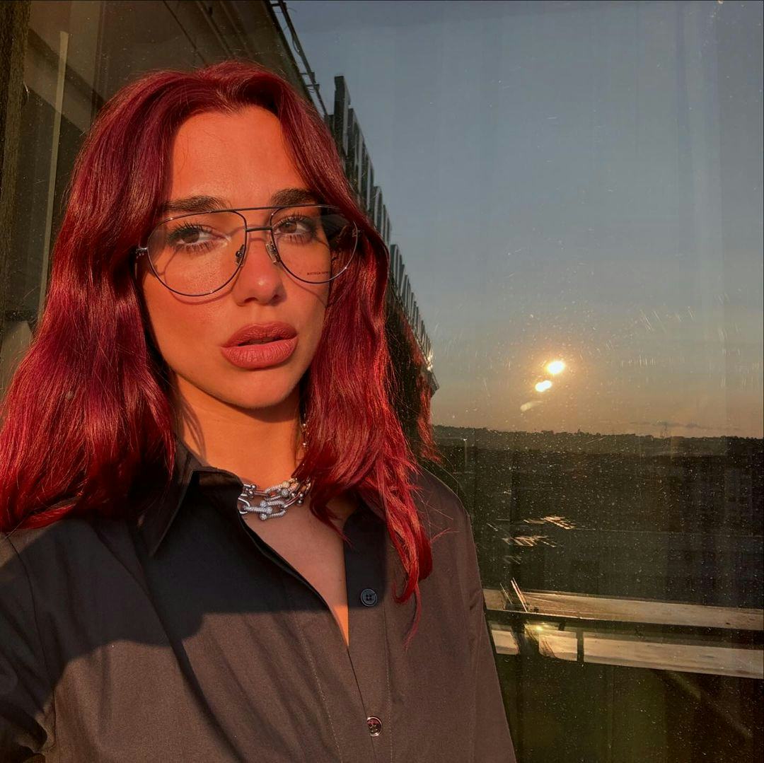 Dua Lipa posing for a selfie wearing Bottega glasses and a silver statement necklace.