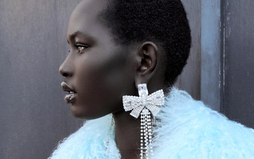 Profile view of a woman wearing a light blue fluffy jacket and a large bow-shaped earring with dangl...