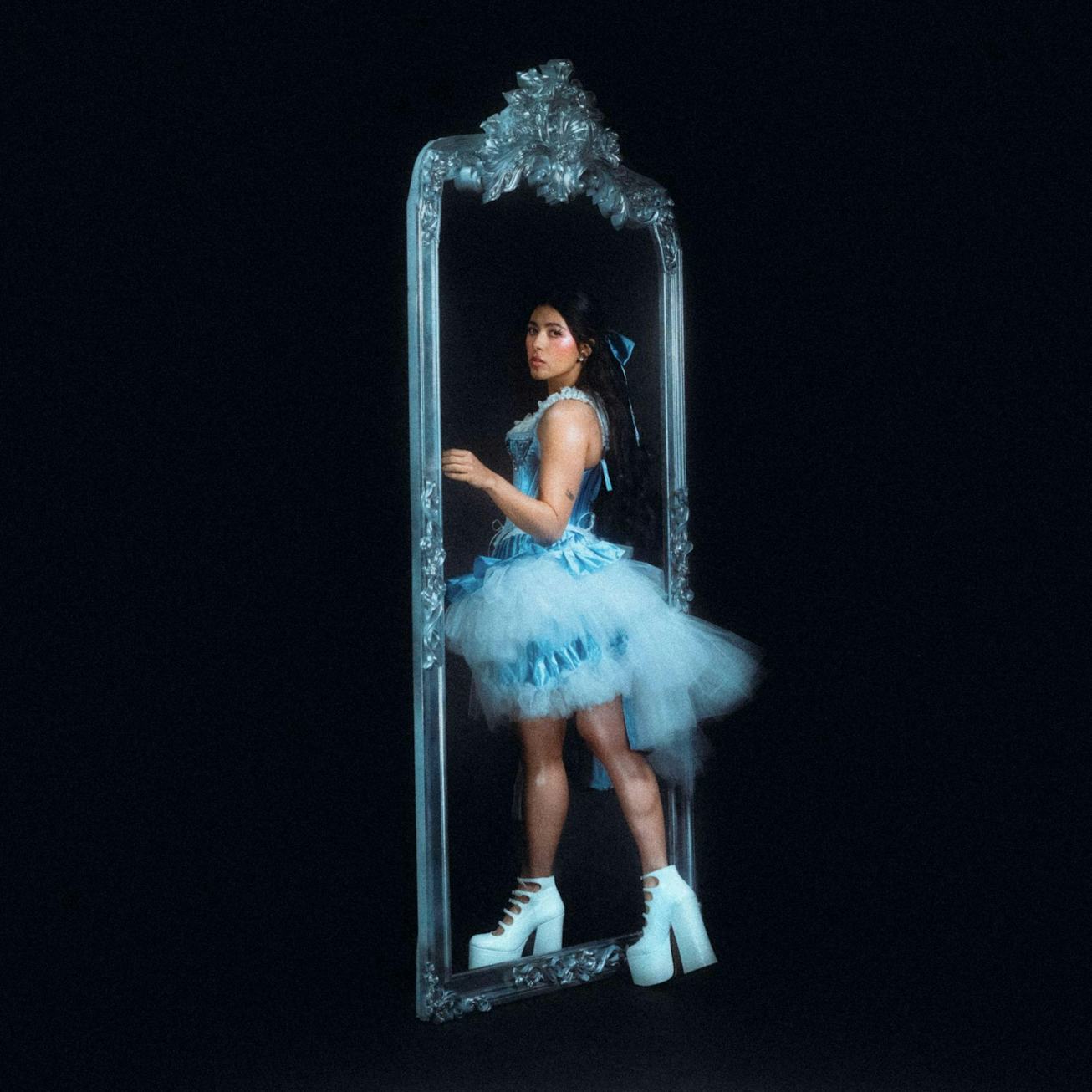 A woman in a blue tutu and white heeled boots poses inside an ornate, vertical mirror set against a ...