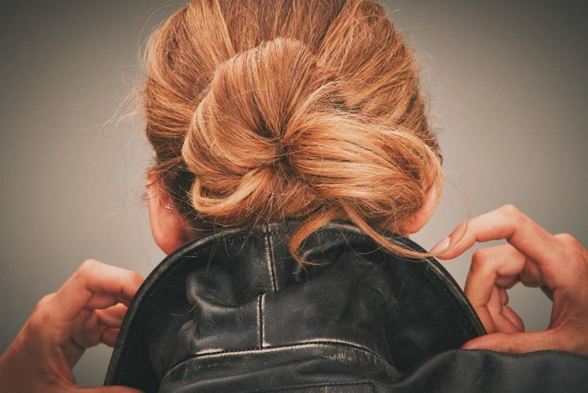 Blake Lively adjusting a black leather jacket, viewed from behind focusing on an elegant bun hairsty…