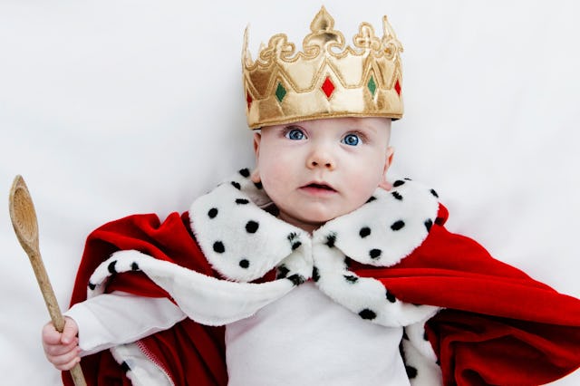 Baby dressed as a king with a crown and royal cloak, holding a wooden spoon, looking surprised again...