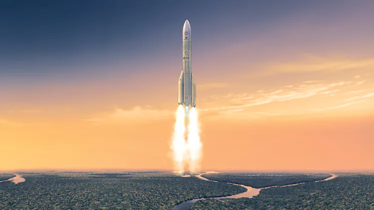 A tall rocket with two boosters at the bottom lifts off from a rainforest, whose lush vegetation sur...