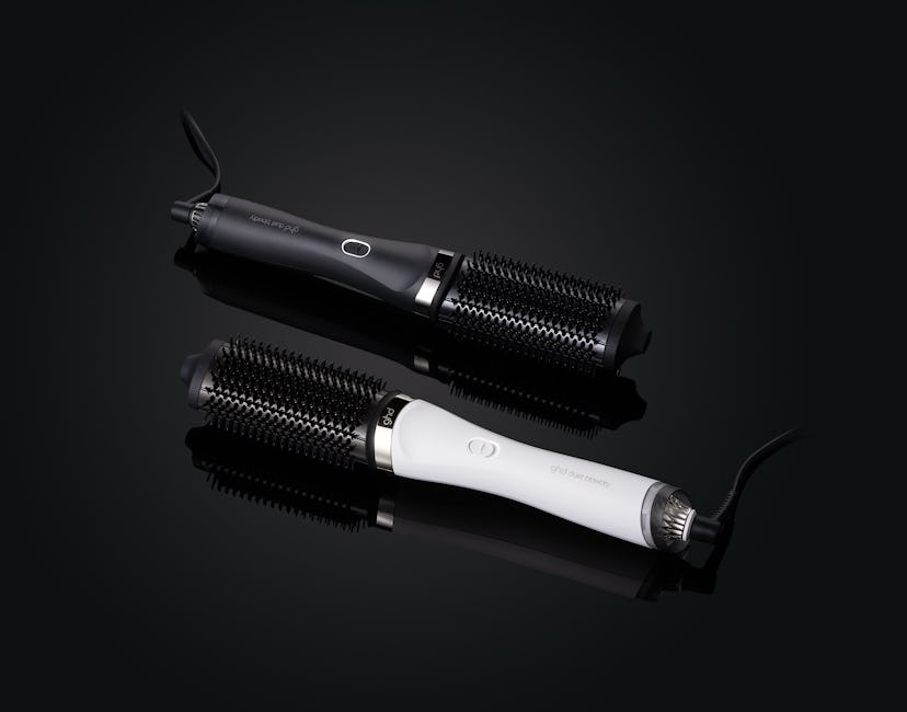 Two round hair styling brushes with handles, one black and one white, on a reflective dark surface.