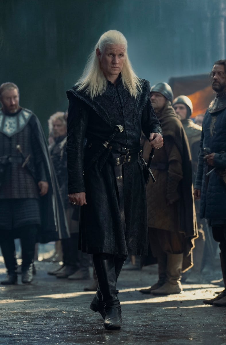 A character with long white hair and black armor stands among a group of armored medieval soldiers i...