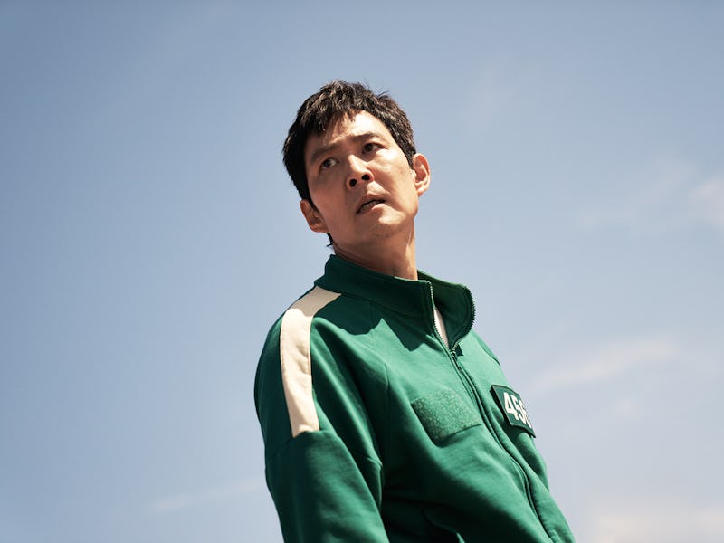 A young man in a green tracksuit looks upwards against a clear blue sky, displaying a serious expres...