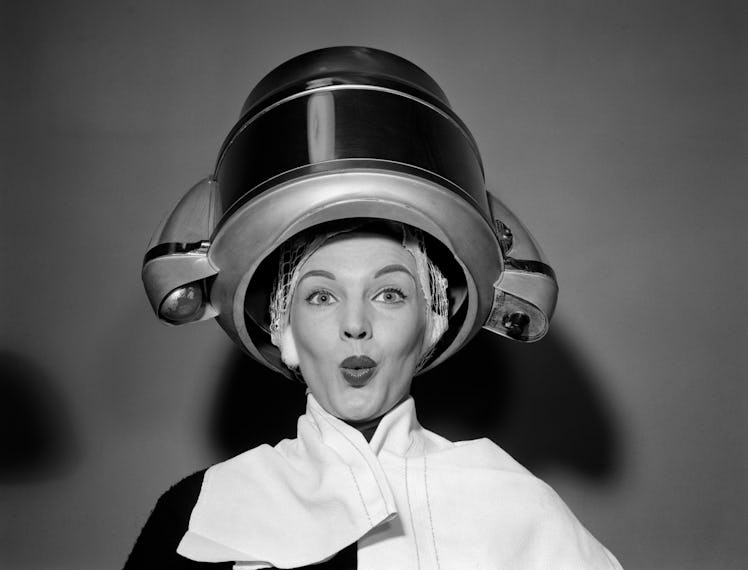 1950s WOMAN UNDER HAIR DRYER WITH TOWEL ON SHOULDERS AND HAIR NET LOOKING AT CAMERA (Photo by Debroc...