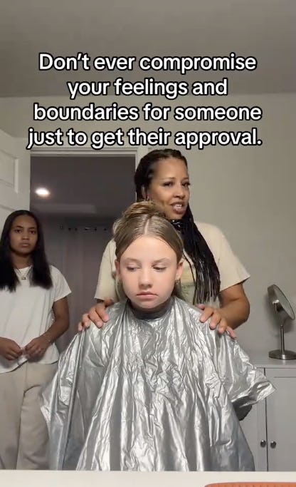 A girl in a salon chair wears a silver cape, looking serious. A woman stands behind her, speaking, while another girl watches in the background.