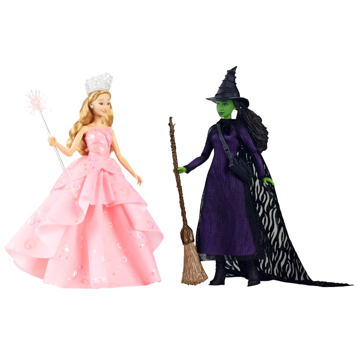 Two dolls stand side by side: one in a pink gown holding a wand, and the other in a black dress with...