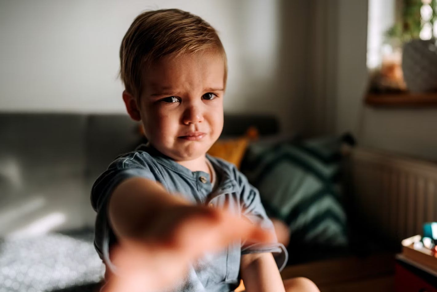 A crying toddler reaching towards the camera.