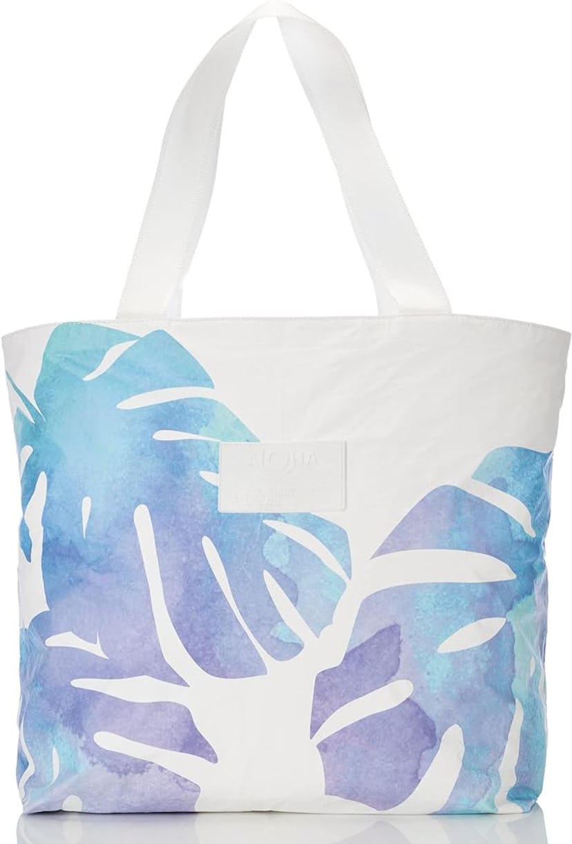 A large tote bag featuring a white background with watercolor-style blue and purple tropical leaf pa...