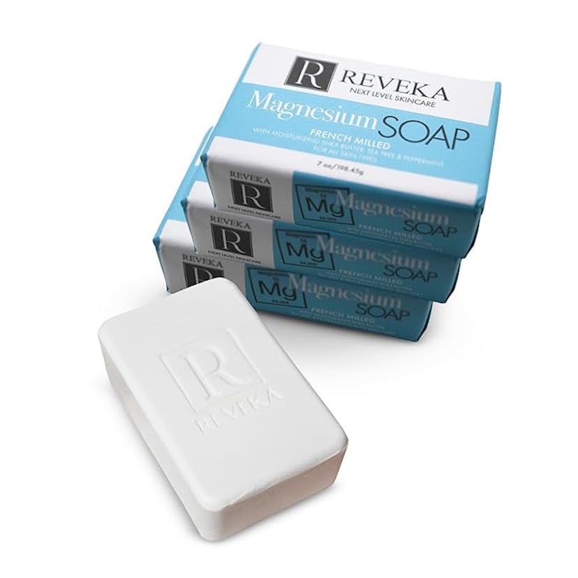 A stack of three boxes of Reveka Magnesium Soap with a white bar of soap in front. The packaging fea...