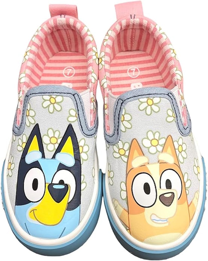 A pair of children's slip-on shoes featuring cartoon dog characters on a light gray background adorn...