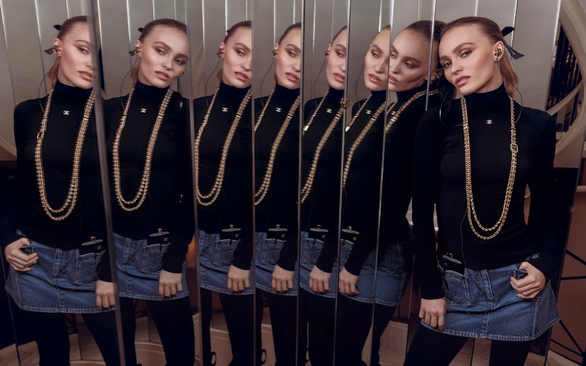 A stylish individual poses in front of mirrored panels, wearing a black turtleneck, denim skirt, and...