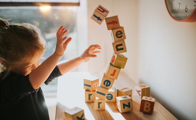 A child plays with colorful wooden blocks, enthusiastically tossing them in the air. Sunlight filter...