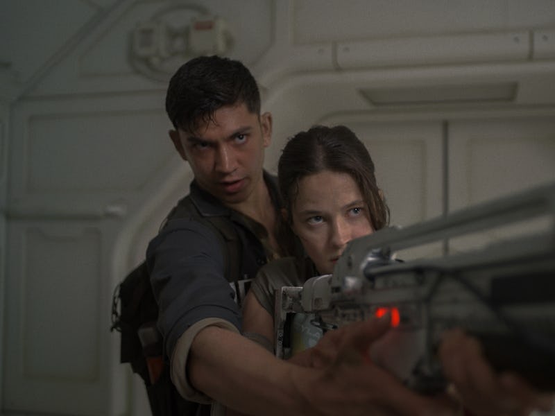 A tense scene featuring a man and a woman in a futuristic setting. The woman aims a weapon while the...