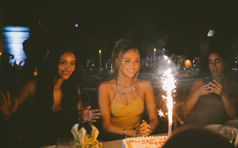 A festive scene at a birthday celebration with two women joyfully reacting to a cake with a sparkler...
